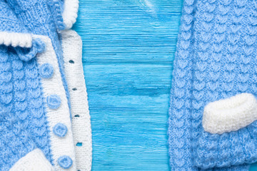 Blue winter knitted baby clothes on blue wooden table background.