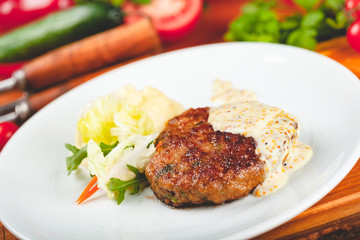 Meat cutlet with mustard sauce served with green salad on white plate.