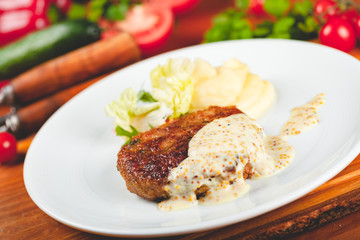 Meat cutlet with mustard sauce served with green salad on white plate.