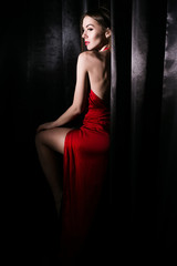 beautiful young woman in red dress with red lips near black curtains 