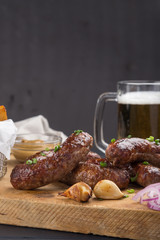 Grilled sausages from a BBQ served with a mustard, fried potatoes, garlic, herbs, beer on a wooden board all served on a black wooden table. Delicious german sausages Perfect for Octoberfest.