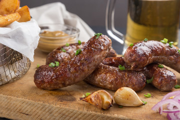 Grilled sausages from a BBQ served with a mustard, fried potatoes, garlic, herbs, beer on a wooden board all served on a black wooden table. Delicious german sausages Perfect for Octoberfest.