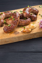 Grilled sausages from a BBQ served with a mustard, fried potatoes, garlic, herbs, beer on a wooden board all served on a black wooden table. Delicious german sausages Perfect for Octoberfest.