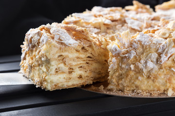 Homemade cake Napoleon on a black table. Free space for text. View from above. Top view. A piece of homemade cake Napoleon on a black table.  piece of Napoleon cake. Cake of puff pastry with sweet