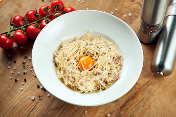 Homemade and fresh carbonara pasta with yolk and parmesan. Italian appetizing spaghetti in white plate on a rustic background in a composition with ingredients. Tasty food
