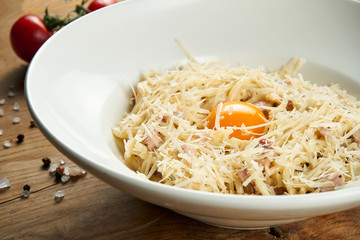 Homemade and fresh carbonara pasta with yolk and parmesan. Italian appetizing spaghetti in white plate on a rustic background in a composition with ingredients. Tasty food