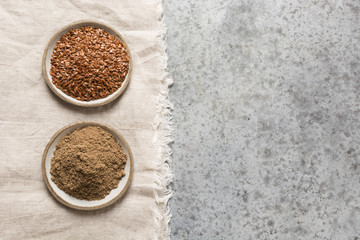 Ground brown flax seed or linseedin bowls on grey stone table. Top view. Space for text.