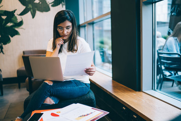 Pensive female freelancer reading finance report and analyzing income from online business working...