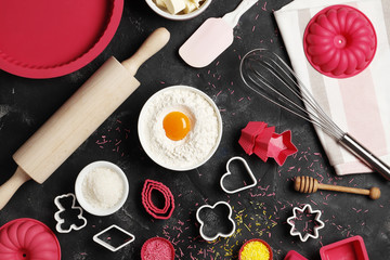 Baking utensils and ingredients. Colorful silicone cooking utensils, rolling pin, cookie mold,.  cupcake cases and sugar sprinkling on a dark background. Easter concept.