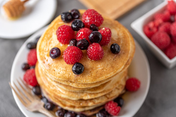 Sweet homemade pancakes with raspberries and blueberries on white plate.