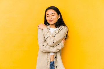 Young chinese woman isolated on a yellow background hugs, smiling carefree and happy.