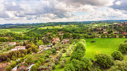 Fototapeta na wymiar Amazing panoramic aerial view above italy countryside with oak forests and green valley rural settlements between trees and meadows with dramatic sky and green pastel colored fields