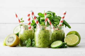 Jars with green smoothie and red tubules on a light background. Freshly made vegetable smoothie. Close-up. Glass jars with green smoothies in a row.