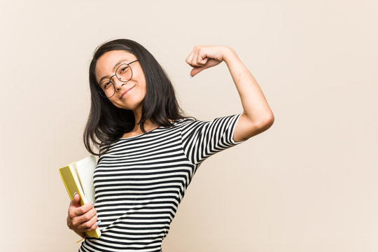 Young asian woman student holding a book raising fist after a victory, winner concept.
