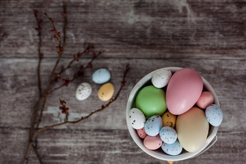 Easter eggs of different sizes are painted in pastel color. Multi-colored Easter eggs in a white bowl on a wooden background. Top view