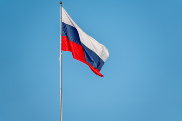 Russian tricolor flag waving in the wind against a blue sky.