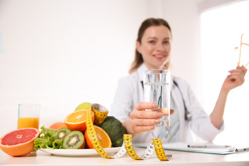 Nutritionist with glass of water, fruits, vegetables and measuring tape in office