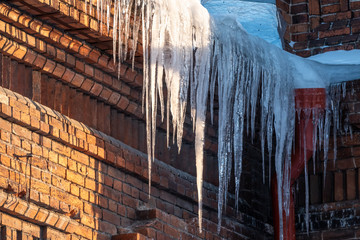 Large icicles hanging from the roof of an old brick house