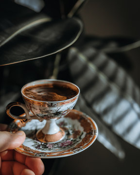 Hand holding a cup of turkish coffee in front of a plant
