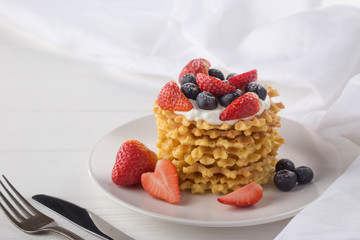 Delicious waffles with fresh fruit and berries on a white wooden table. Waffles with strawberries and blueberries. Free space for text. Traditional belgian waffles with fresh fruit. Stack of waffles w