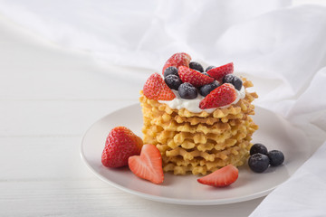 Delicious waffles with fresh fruit and berries on a white wooden table. Waffles with strawberries and blueberries. Free space for text. Traditional belgian waffles with fresh fruit. Stack of waffles w