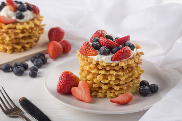 Delicious waffles with fresh fruit and berries on a white wooden table. Waffles with strawberries and blueberries. Free space for text. Traditional belgian waffles with fresh fruit. Stack of waffles w