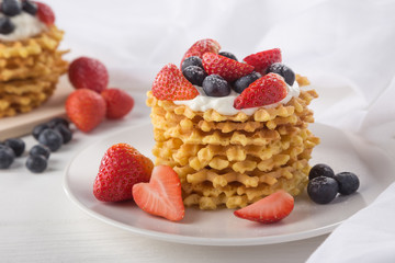 Delicious waffles with fresh fruit and berries on a white wooden table. Waffles with strawberries and blueberries. Free space for text. Traditional belgian waffles with fresh fruit. Stack of waffles w