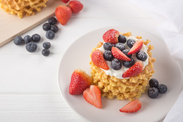 Delicious waffles with fresh fruit and berries on a white wooden table. Waffles with strawberries and blueberries. Free space for text. Traditional belgian waffles with fresh fruit. Stack of waffles w