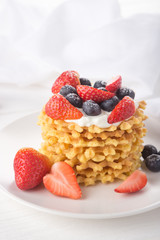 Delicious waffles with fresh fruit and berries on a white wooden table. Waffles with strawberries and blueberries. Free space for text. Traditional belgian waffles with fresh fruit. Stack of waffles w