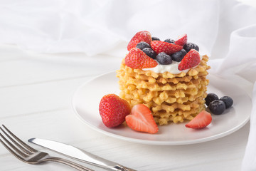 Delicious waffles with fresh fruit and berries on a white wooden table. Waffles with strawberries and blueberries. Free space for text. Traditional belgian waffles with fresh fruit. Stack of waffles w