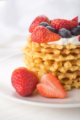 Delicious waffles with fresh fruit and berries on a white wooden table. Waffles with strawberries and blueberries. Free space for text. Traditional belgian waffles with fresh fruit. Stack of waffles w