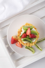 Delicious waffles with fresh fruit and berries on a white wooden table. Waffles with strawberries, kiwi, banana, cream. Free space for text. Traditional belgian waffles with fresh fruit. Stack of waff