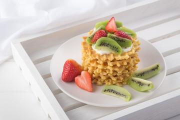 Delicious waffles with fresh fruit and berries on a white wooden table. Waffles with strawberries, kiwi, banana, cream. Free space for text. Traditional belgian waffles with fresh fruit. Stack of waff