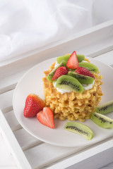 Delicious waffles with fresh fruit and berries on a white wooden table. Waffles with strawberries, kiwi, banana, cream. Free space for text. Traditional belgian waffles with fresh fruit. Stack of waff
