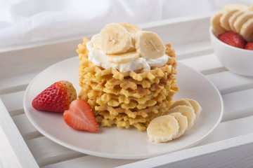 Delicious waffles with fresh fruit and berries on a white wooden table. Waffles with strawberries, kiwi, banana, cream. Free space for text. Traditional belgian waffles with fresh fruit. Stack of waff