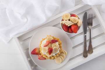 Delicious waffles with fresh fruit and berries on a white wooden table. Waffles with strawberries, kiwi, banana, cream. Free space for text. Traditional belgian waffles with fresh fruit. Stack of waff