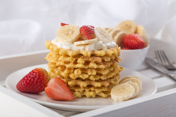 Delicious waffles with fresh fruit and berries on a white wooden table. Waffles with strawberries, kiwi, banana, cream. Free space for text. Traditional belgian waffles with fresh fruit. Stack of waff