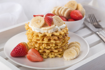 Delicious waffles with fresh fruit and berries on a white wooden table. Waffles with strawberries, kiwi, banana, cream. Free space for text. Traditional belgian waffles with fresh fruit. Stack of waff