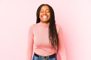 Young african american woman isolated on a pink background laughs and closes eyes, feels relaxed and happy.