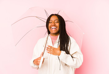 Young african american woman holding an umbrella isolated laughs out loudly keeping hand on chest.