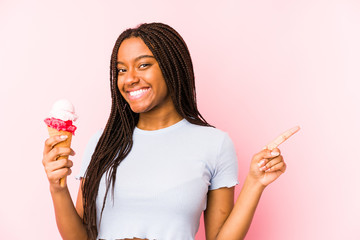 Young african american woman holding an ice cream isolated smiling and pointing aside, showing...