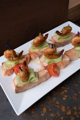 Shrimp on the cucumber and red salmon with cherry tomatoes. White plate. Rusty metal background.