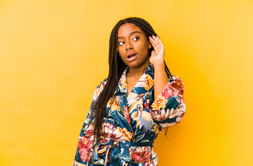 Young african american woman wearing an asiatic pijama isolated trying to listening a gossip.