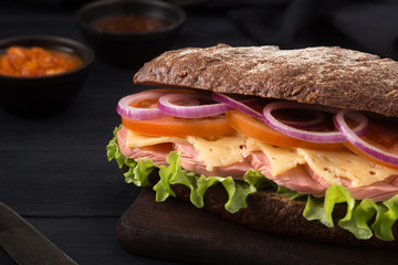 Delicious sandwich on a black wooden table. Sandwich with meat, ham, cheese, lettuce, tomatoes, onion, sauce. Close-up shot. Sandwich bread tomato, lettuce and yellow cheese. Free space for text.