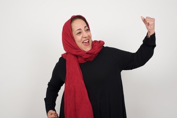 Attractive young caucasian woman celebrating a victory punching the air with her fists and a beaming toothy smile over a white studio background with copy space.