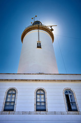 Fototapeta na wymiar Sun hiding behind a white lighthouse near to the beach of Malaga. Andalusia. Spain. 