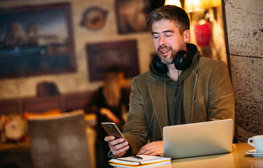 Middle-aged handsome man listening music using headphones and laptop at cafe.