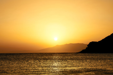 Fototapeta na wymiar Landscape of a golden sunset in a beach in the Mediterranean. Sun disappearing behind the mountains.