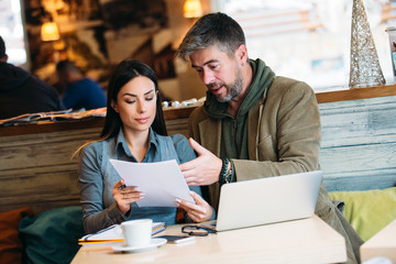 Portrait of young business man and woman at cafe discussing contract.
