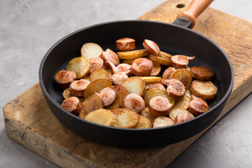 Close-up shot of fried potatoes with sausages and egg. Breakfast. Potatoes with sausages, cut into slices and fried in oil, in rustic style. Frying pan with tasty cooked egg and sausages on table